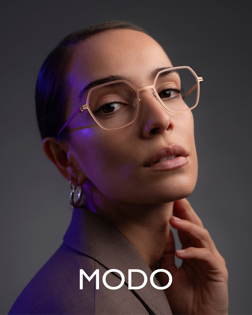 MODO Eyewear campaign featuring female model in nude acetate/titanium eyeglasses with plain grey background – luxury women’s eyewear fashion photography.